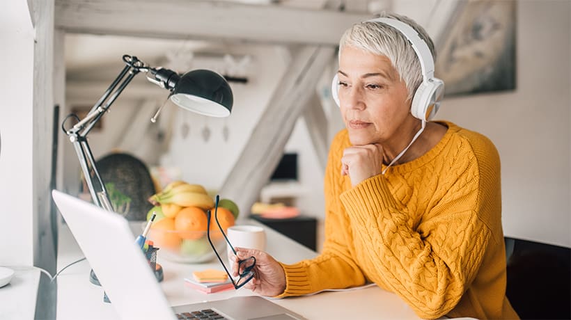 Vrouw met gele trui en koptelefoon kijkt naar laptop