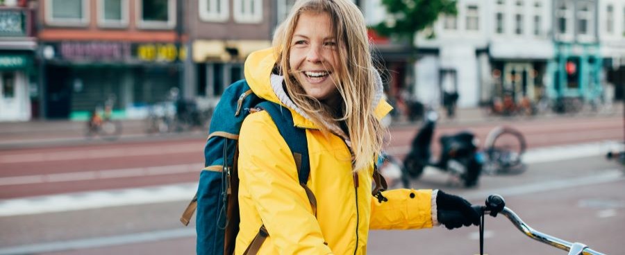 Een afbeelding van een lachende vrouw in een gele jas die op de fiets zit. 