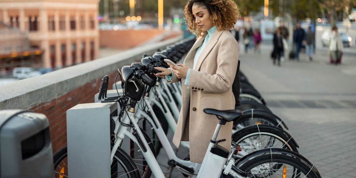 Een vrouw kijkt op haar telefoon bij e-bike om haar privévervoer te verduurzamen