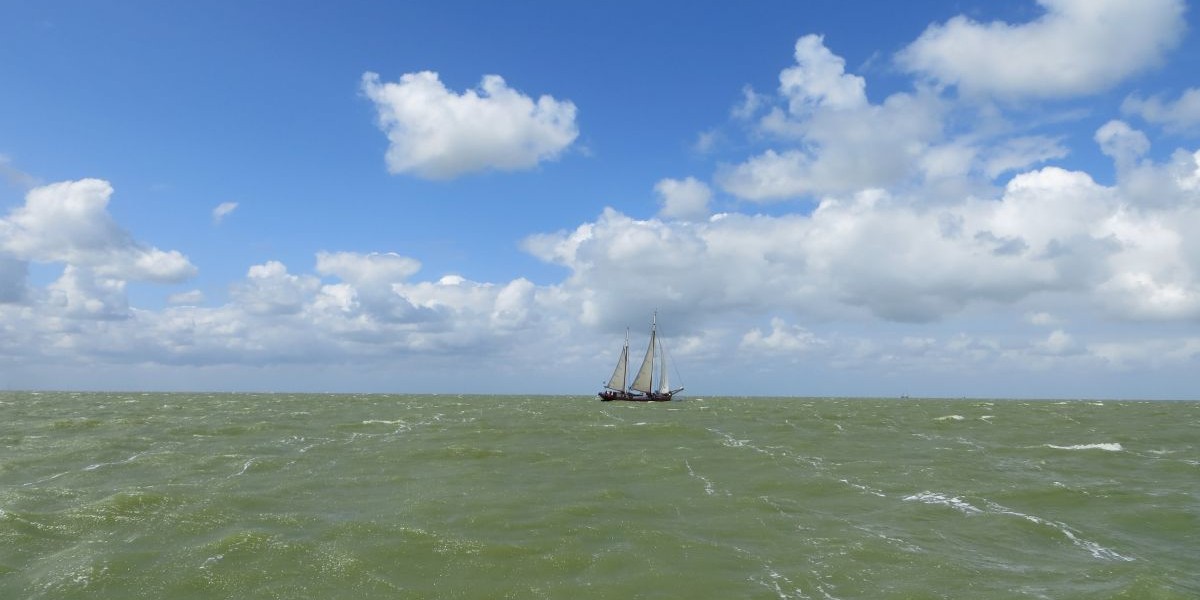 Een schip in de verte onder een blauwe lucht met wolken