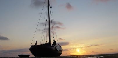 Een zeilboot met op de achtergrond een zonsondergang 