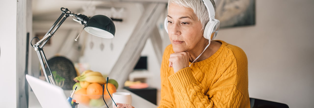 Vrouw met gele trui en koptelefoon kijkt naar laptop