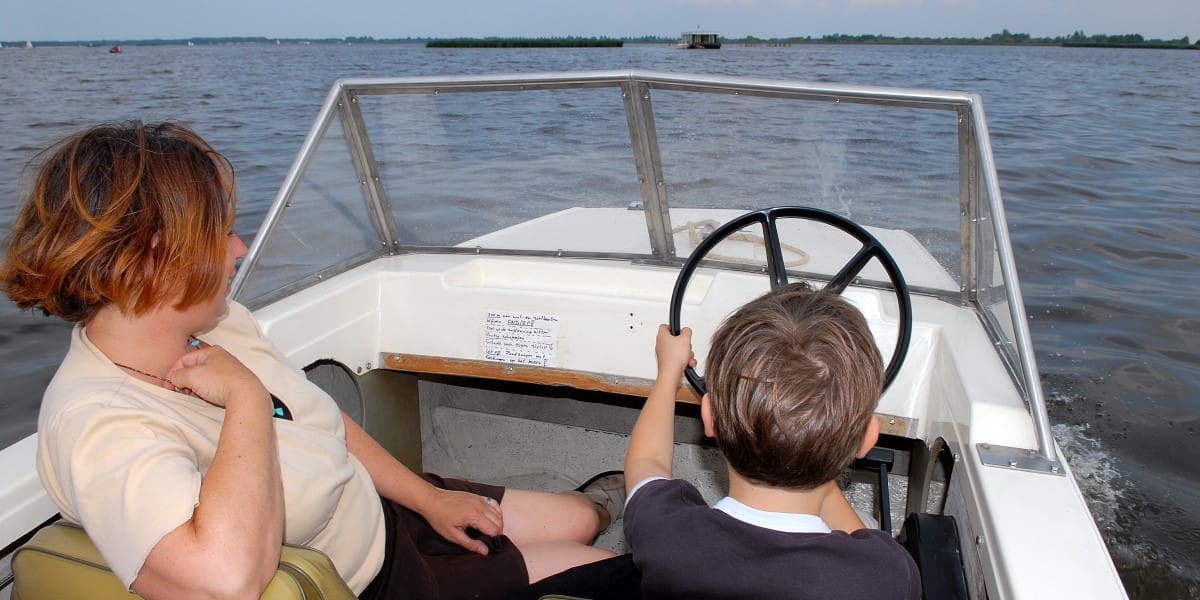 Een moeder en zoon op een boot. Het jongetje zit achter het stuur 